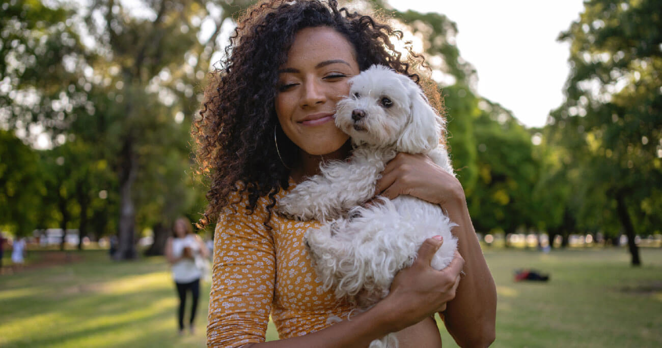 A woman cuddling a small white dog outdoors.